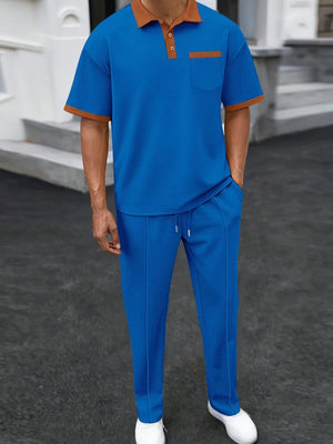Trendbye wearing a blue outfit with brown accents standing on a dark surface.