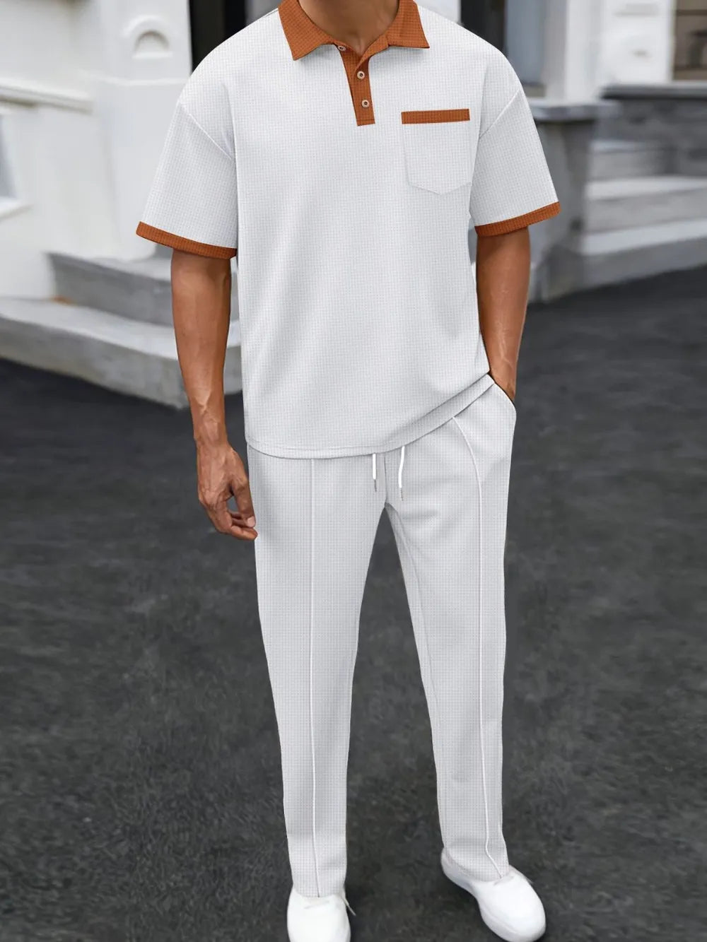 Trendbye wearing a white polo shirt with brown accents and white pants on a dark surface.