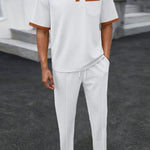 Trendbye wearing a white polo shirt with brown accents and white pants on a dark surface.