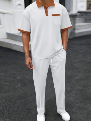 Trendbye wearing a white polo shirt with brown accents and white pants on a dark surface.